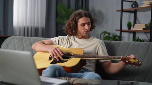 Jeune homme adulte passant du temps à la maison Un homme est assis sur le canapé avec la fixation et le réglage de la guitare acoustique