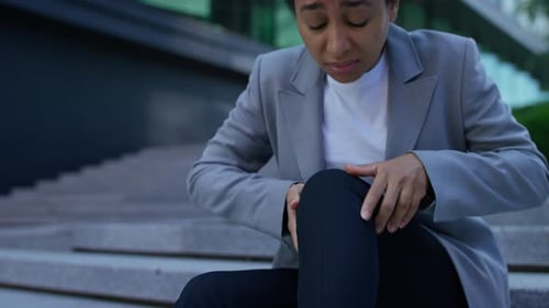 Woman Massaging Knee in Pain Sitting on Steps