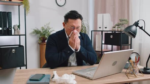 Businessman Suffers From Cold Flu Fever or Allergy Sneezes Wipes Snot Working on Laptop at Office