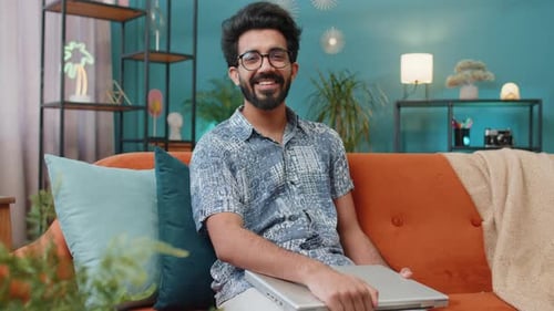 Un travailleur indépendant indien assis sur un canapé fermant son ordinateur portable après avoir fini de travailler dans le salon à la maison
