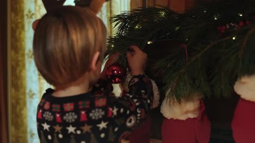 Child Decorates Christmas Tree with Red Ornaments