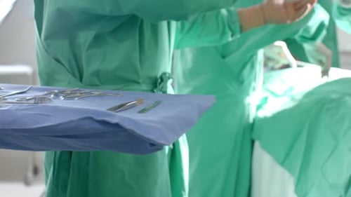 Diverse surgeons wearing surgical gowns operating on patient in operating theatre, slow motion