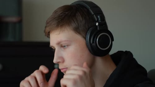 Young man wearing headphones and focusing on sound, producing music, mixing, and mastering audio