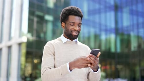 Smiling african american businessman using a mobile phone while standing on street near a modern