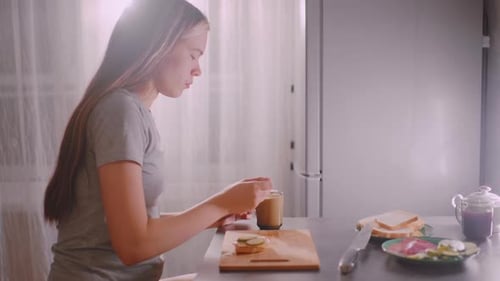 Woman Prepares Sandwich and Stirring Beverage in Kitchen