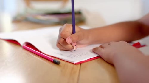 African American teen gripping purple pencil, steadying red notebook on wood table, doing homework
