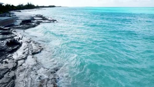 aerial view along a white beach further out over the turquoise blue sea. the waves are breaking on t