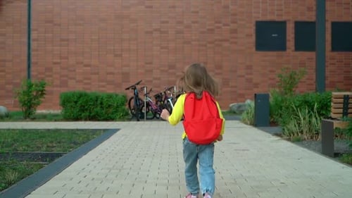 Preschooler Girl Runs and Jumps with School Backpack in School Yard Education