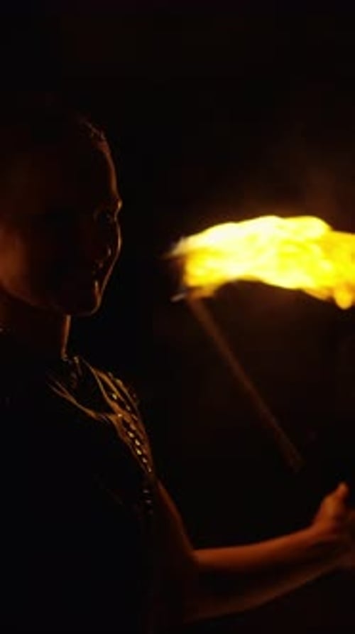 Silhouetted Performer Moving Beside Vivid Flames in Deep Darkness Illuminated By Subtle Firelight