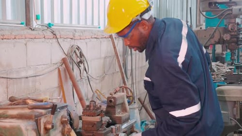 Young black engineer man operating lathe machine for preparing production at factory.