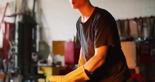 Professional metalsmith works red hot metal with tools in dark blacksmith workshop