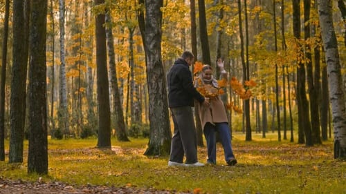 Happy Young Couple with Dog Tossing Autumn Leaves into Air in Forest Park