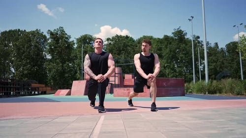 Personal fitness trainer training athlete on sports field Two active sweaty guys stretching legs