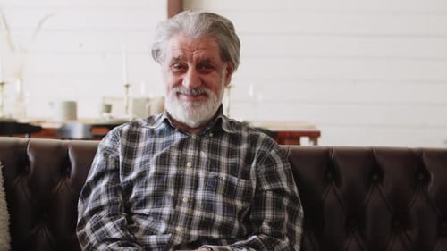 Smiling Handsome Older Man Looking at Camera While Sitting on Couch at Home Feeling Happy Concept