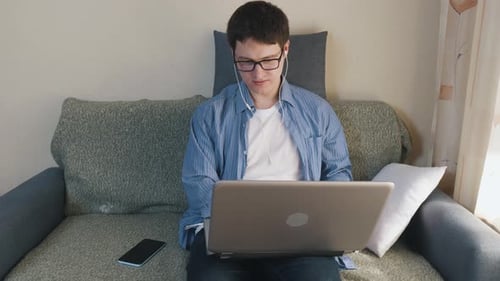 Young Adult Uses Laptop on Couch at Home
