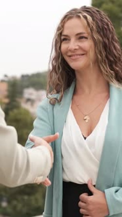 Businesswomen Engaging in a Handshake Outdoors Amidst a Cityscape Vertical