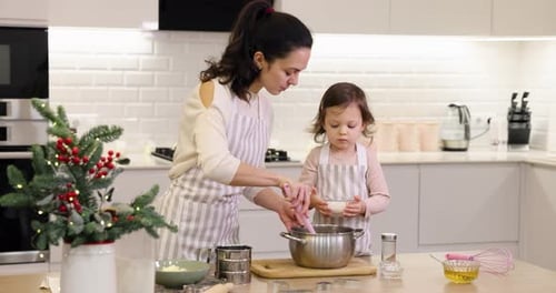 Mother and Her Little Child Daughter in Aprons Preparing the Dough in the Kitchen