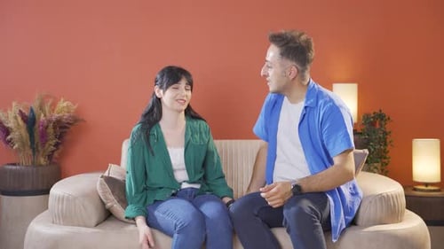 Woman Joins Man Sitting On Couch at Home