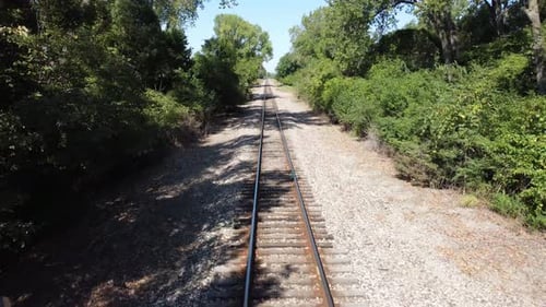 Drohne, die tagsüber über eine Brücke und durch die Bäume fährt und den Bahngleisen folgt.