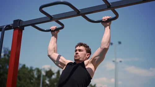 portrait of a young sweaty sportsman doing horizontal bar swings arms and shoulders push-ups