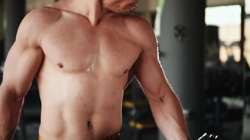 Iluminando halteres e treinando bíceps. Jovem esportivo sem camisa e forte faz um dia de treino na academia