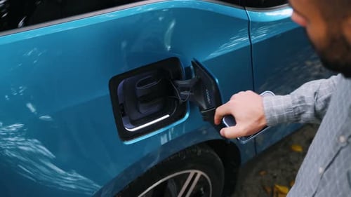 Young man charging electric car outdoor at green forest. Save ecology alternative energy sustainable