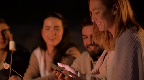 Friends enjoying campfire marshmallows and selfies on a summer beach night