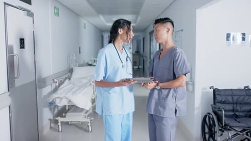 Diverse doctor and nurse using tablet and talking in corridor at hospital, in slow motion