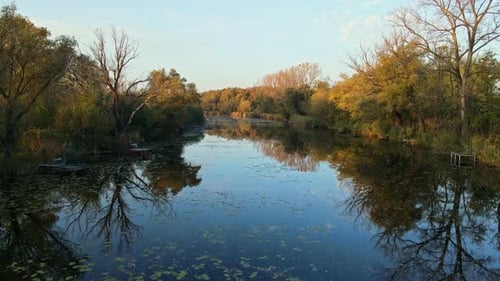 Flying with a drone over a serene river surrounded by autumnal trees with golden and green foliage.
