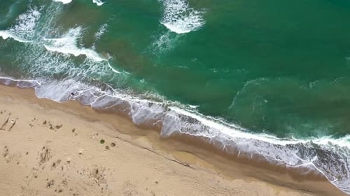 Flying over a tropical coast with sea waves washing sandy beach. Aerial drone view