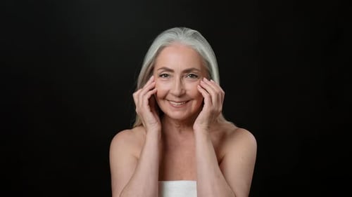 Senior Woman With Light Skin Smiling While Touching Her Face in Studio Setting