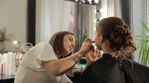 Woman Applies Makeup to Another in Beauty Studio