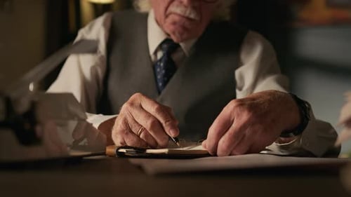 Hände eines nachdenklichen reifen Schriftstellers, der sich am Schreibtisch Notizen macht