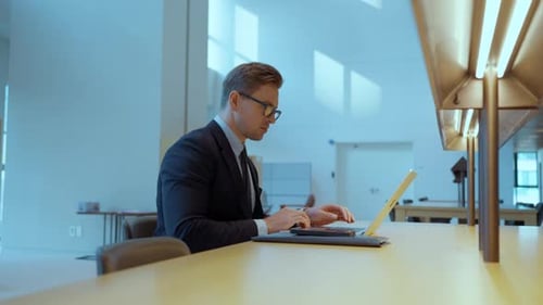Handsome blond businessman sitting alone in the office and using laptop computer - side view
