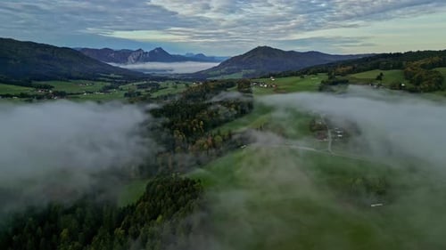 Luftdrohnenaufnahme über weiße Wolken, die über einer Bergstadt entlang des Gebirgstals bedeckten W