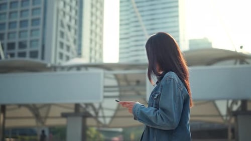 Happy asian woman with smile walking and using smartphone on the street in urban city