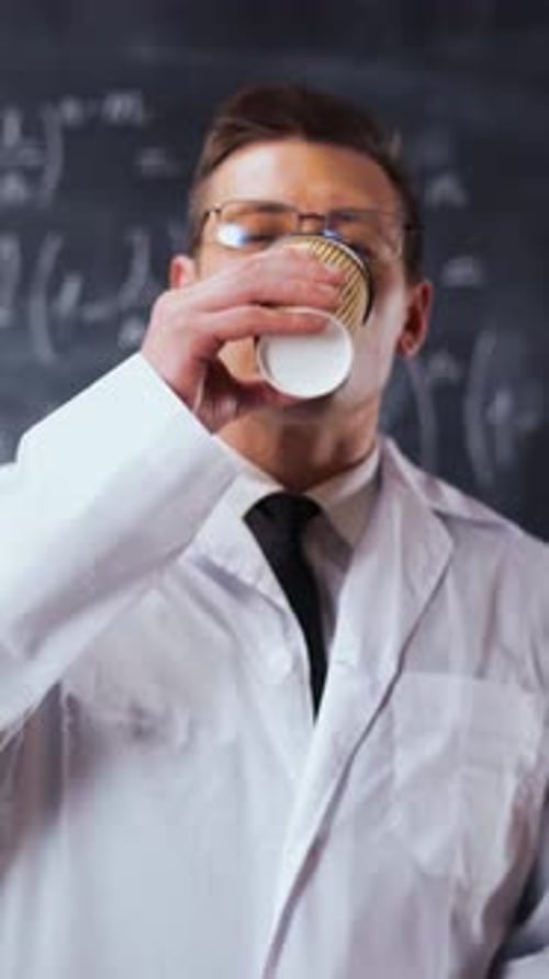 Vertical of Scientist Man in White Work Robe Near Chalk Board with Equations Drinks Coffee
