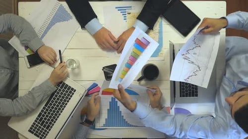 Vista superior de las manos de empresarios sentados a la mesa en una oficina moderna y examinando gráficos, grupo de