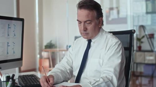 Mature Entrepreneur Working on Report in Office and Looking at Camera