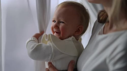 Cute Baby Reaches for Window Curtains Held by Adult
