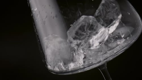 Clear Ice Cubes Falling Into Empty Wineglass On Black Background Close Up. Frozen Blocks Thrown A...