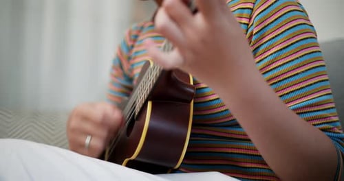 Close-up of woman's hand playing a song on a ukulele.