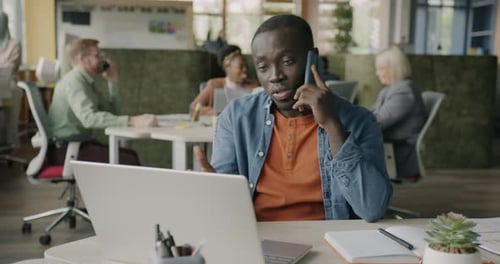 Joyful Entrepreneur Speaking on Mobile Phone Making Call and Working with Laptop in Coworking Center