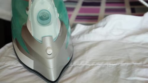 Female Hand Holding Electric Iron Ironing Clothes on Ironing Board