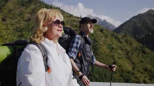 Portrait of a Pensioners with Backpacks and Hiking Sticks Cheerfully Walking on a Road with