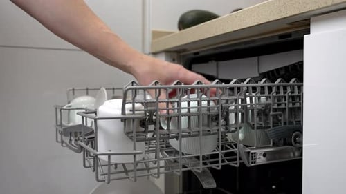 Housewife loading dishes into dishwasher basket in modern kitchen