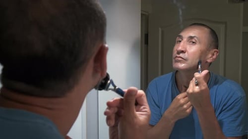 An adult man shaves his face.