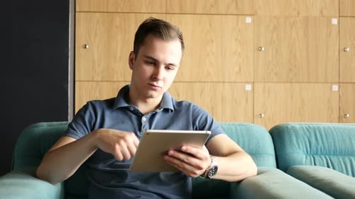Man Sits Using Tablet on Blue Couch