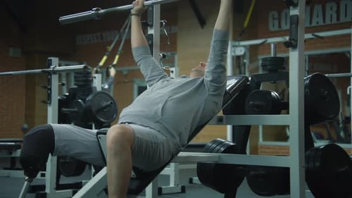 Athlete with Prosthetic Leg Trains with Empty Barbell in Gym
