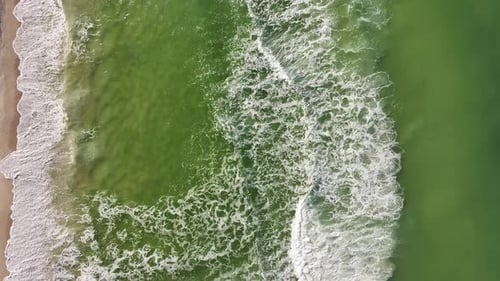 Bird-eye view of ocean waves down below crashing onto the shore in Summer.